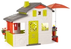 Spielhaus Neo Friends House DeLuxe Smoby Mit Einer Beleuchteten Spielküche Im Inneren Und Einem Essbereich Unter Einem Sonnenschirm